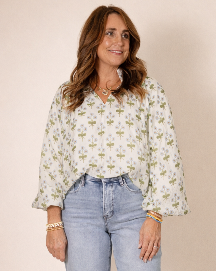 Woman wearing a floral blouse and light blue jeans against a beige background