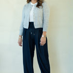 A woman modeling a light gray cardigan over a white top and navy wide-leg drawstring pants, standing against a plain off-white studio background.