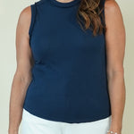 A woman wearing a sleeveless mock neck top in navy blue and white pants, standing against a plain light beige background.