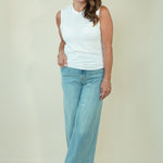 A woman modeling a white sleeveless top and light blue wide-leg jeans against a plain beige studio background.