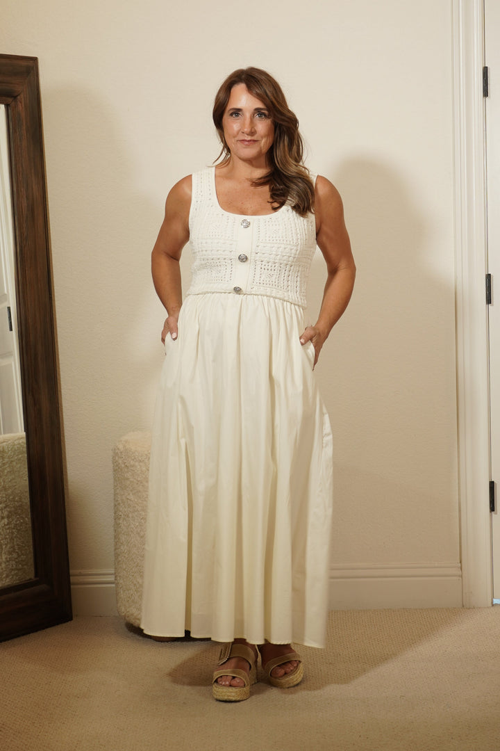 Woman in a white dress standing in front of a mirror in a room with beige walls and a wooden cabinet.