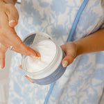 Person holding a jar of cream with a blue and white patterned garment in the background