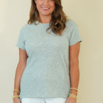A woman modeling a light heather gray short-sleeve t-shirt and white shorts against a plain beige studio background.