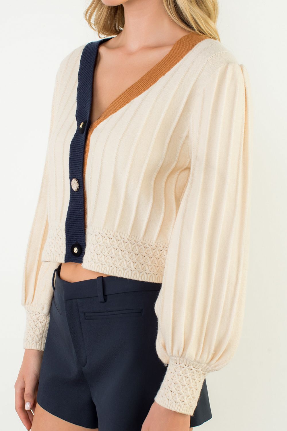 Woman wearing a cream blouse with a V-neck and navy accents, paired with dark pants on a white background.