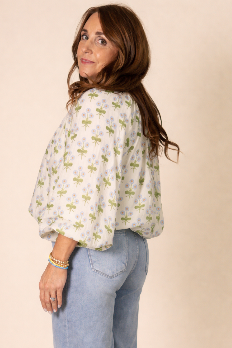Woman wearing a floral blouse and jeans against a beige background