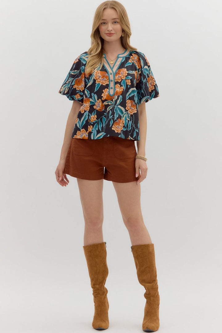 Woman wearing a floral blouse, brown shorts, and tan boots on a white background