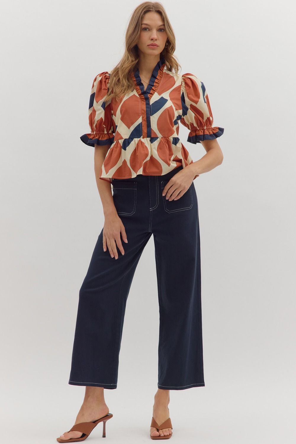Woman wearing a patterned blouse and dark jeans on a white background