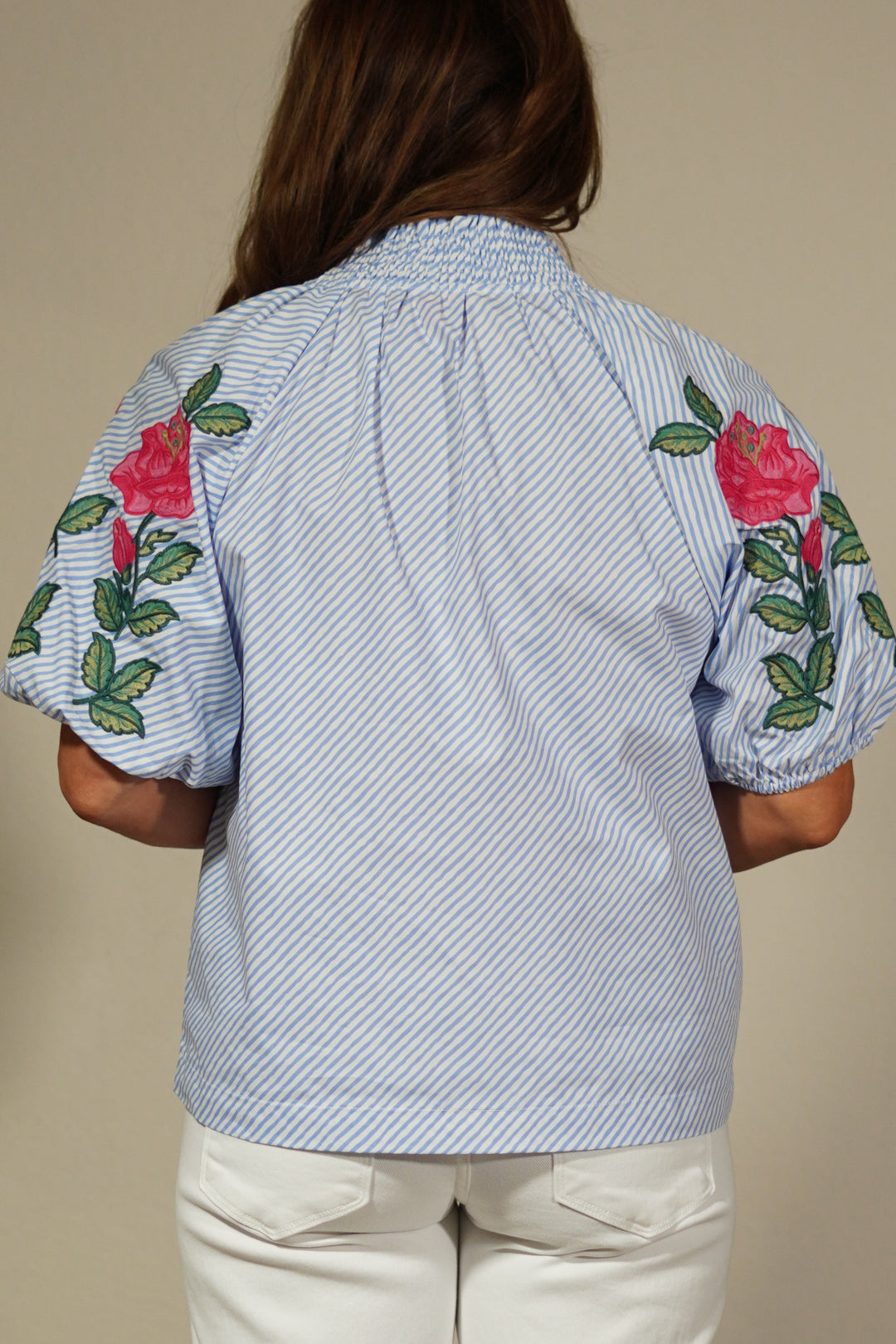 Person wearing a light blue shirt with floral embroidery and beige pants on a plain background