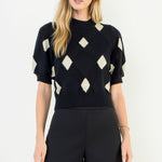 Woman wearing a black and white patterned top with black shorts on a white background