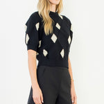 Woman wearing a black and white patterned top with black shorts on a white background