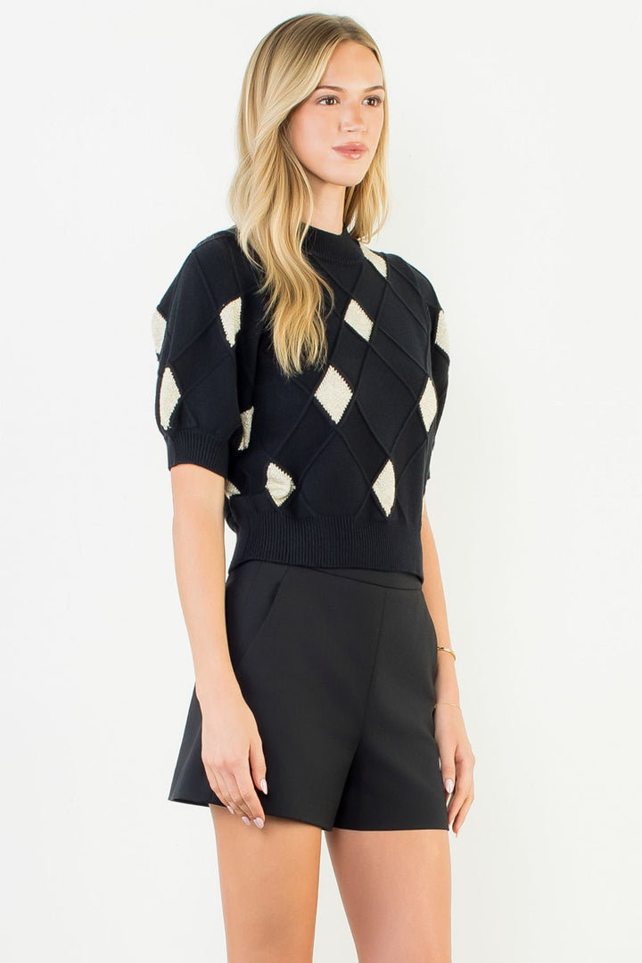 Woman wearing a black and white patterned top with black shorts on a white background