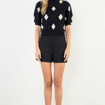 Woman wearing a black and white patterned top with black shorts on a white background