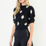 Woman wearing a black and white patterned top with black shorts on a white background