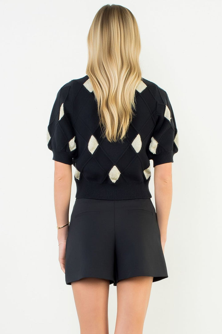 Person wearing a black sweater with white diamond patterns and black shorts on a white background