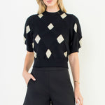 Woman wearing a black and white patterned top with black shorts on a white background