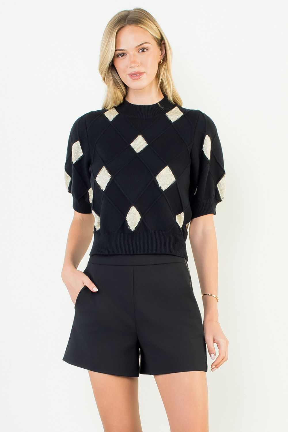 Woman wearing a black and white patterned top with black shorts on a white background