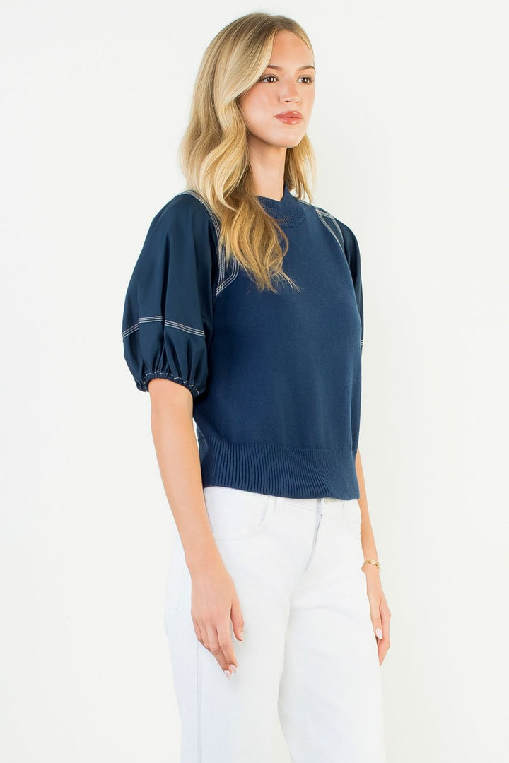 Woman wearing a navy blue sweater with white pants on a white background