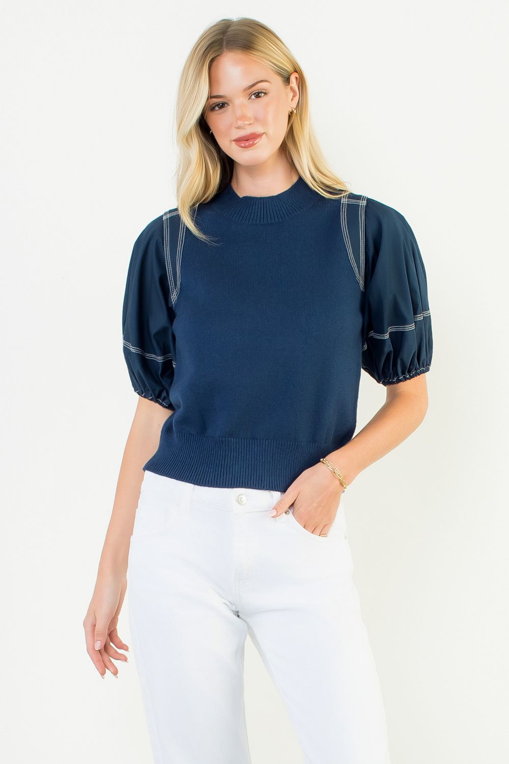 Woman wearing a navy blue sweater with puff sleeves on a white background