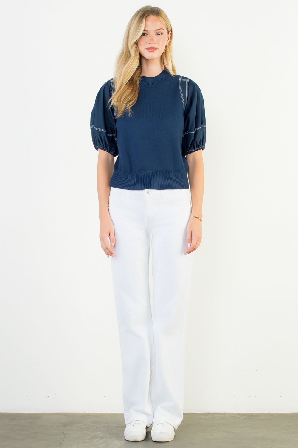 Woman wearing a navy blue top and white pants on a plain background