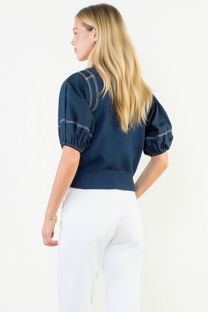 Woman wearing a navy blue top with puff sleeves on a white background