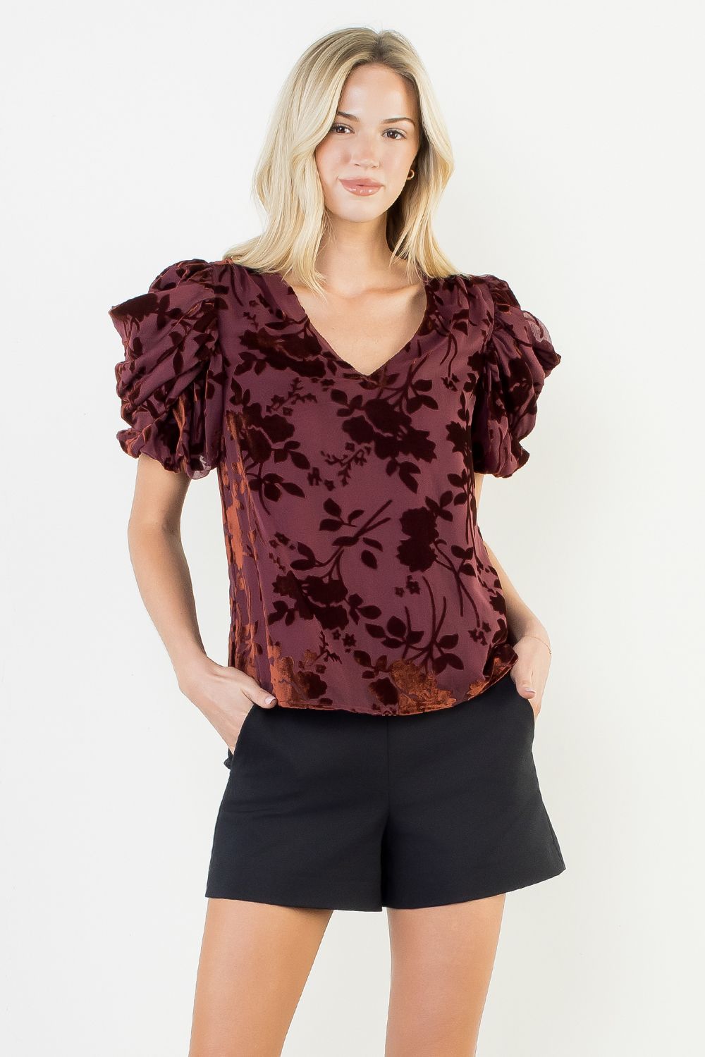 Woman wearing a burgundy floral blouse and black shorts on a white background