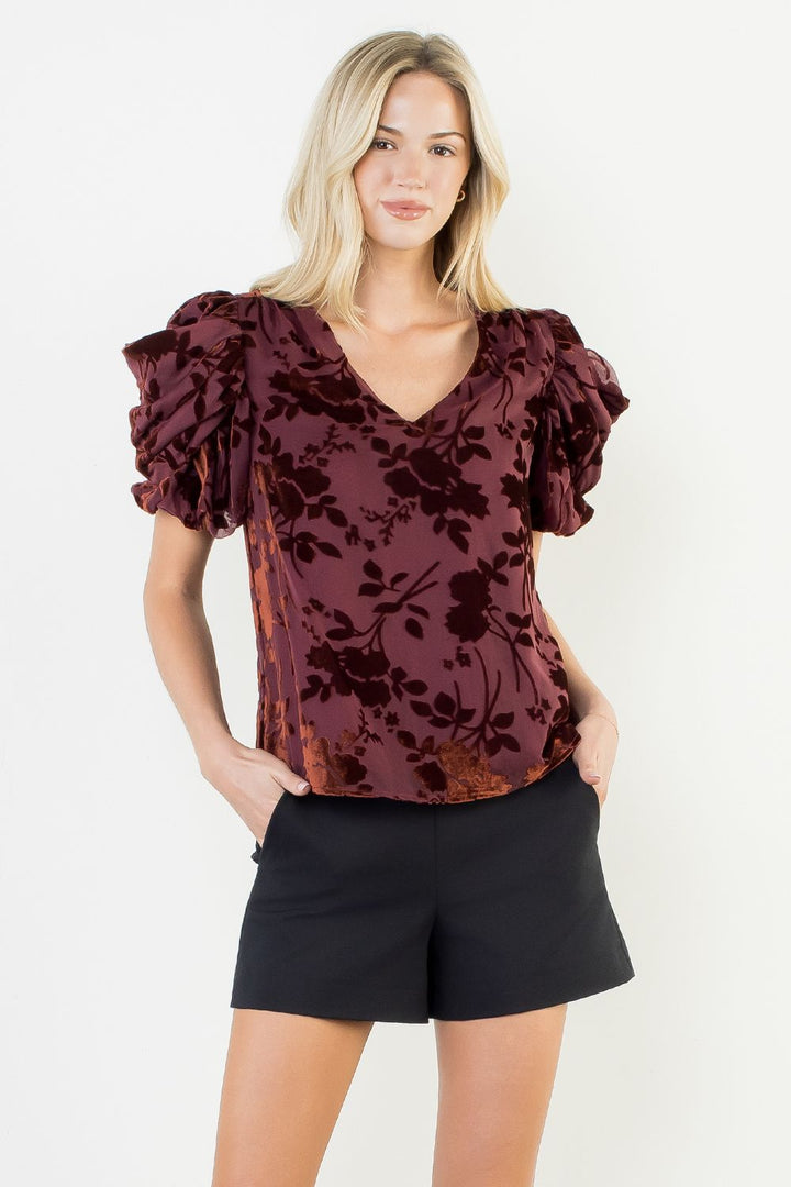 Woman wearing a burgundy floral blouse and black shorts on a white background