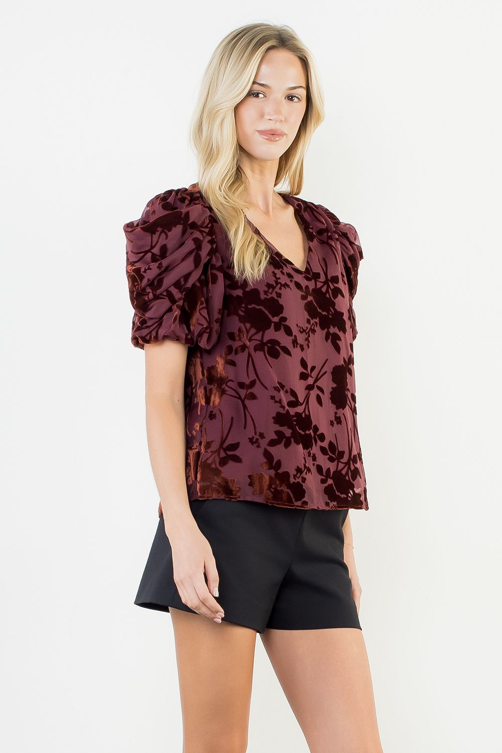 Woman wearing a burgundy floral blouse and black shorts on a white background
