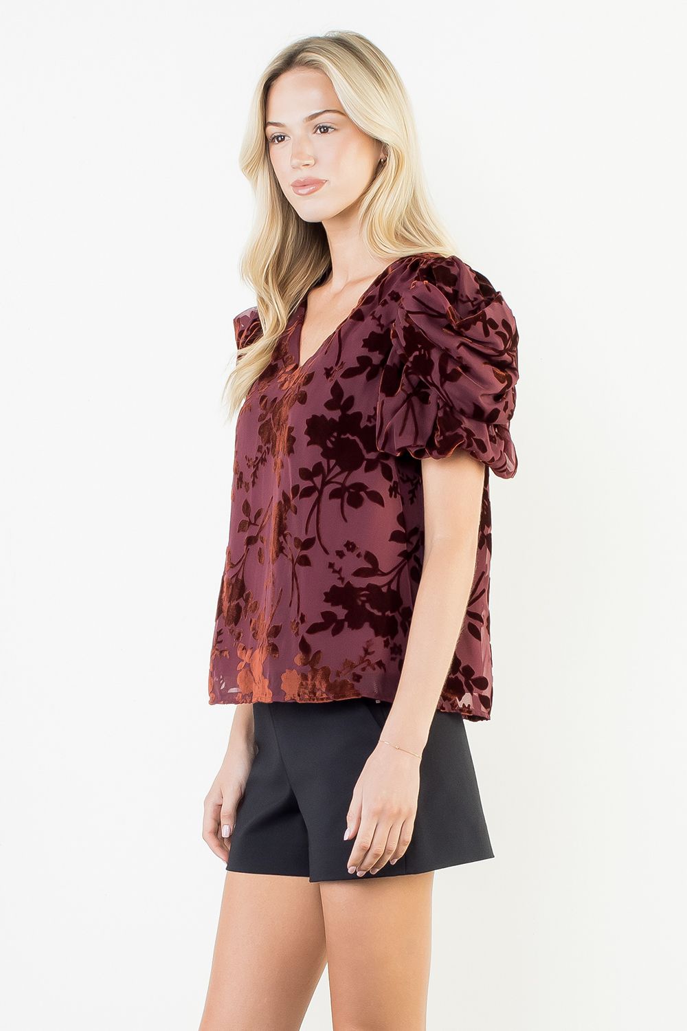 Woman wearing a burgundy floral blouse with black shorts on a white background