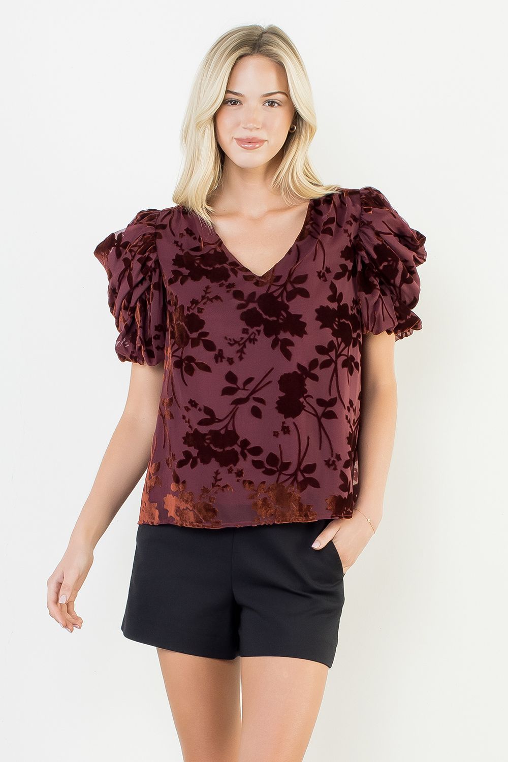 Woman wearing a burgundy floral blouse with ruffled sleeves on a white background