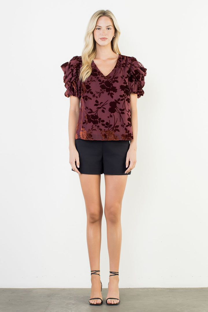 Woman wearing a burgundy floral blouse and black shorts on a white background