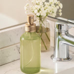 Green spray bottle with gold nozzle on a white surface