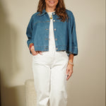Woman wearing a denim jacket and white pants standing in front of a mirror.