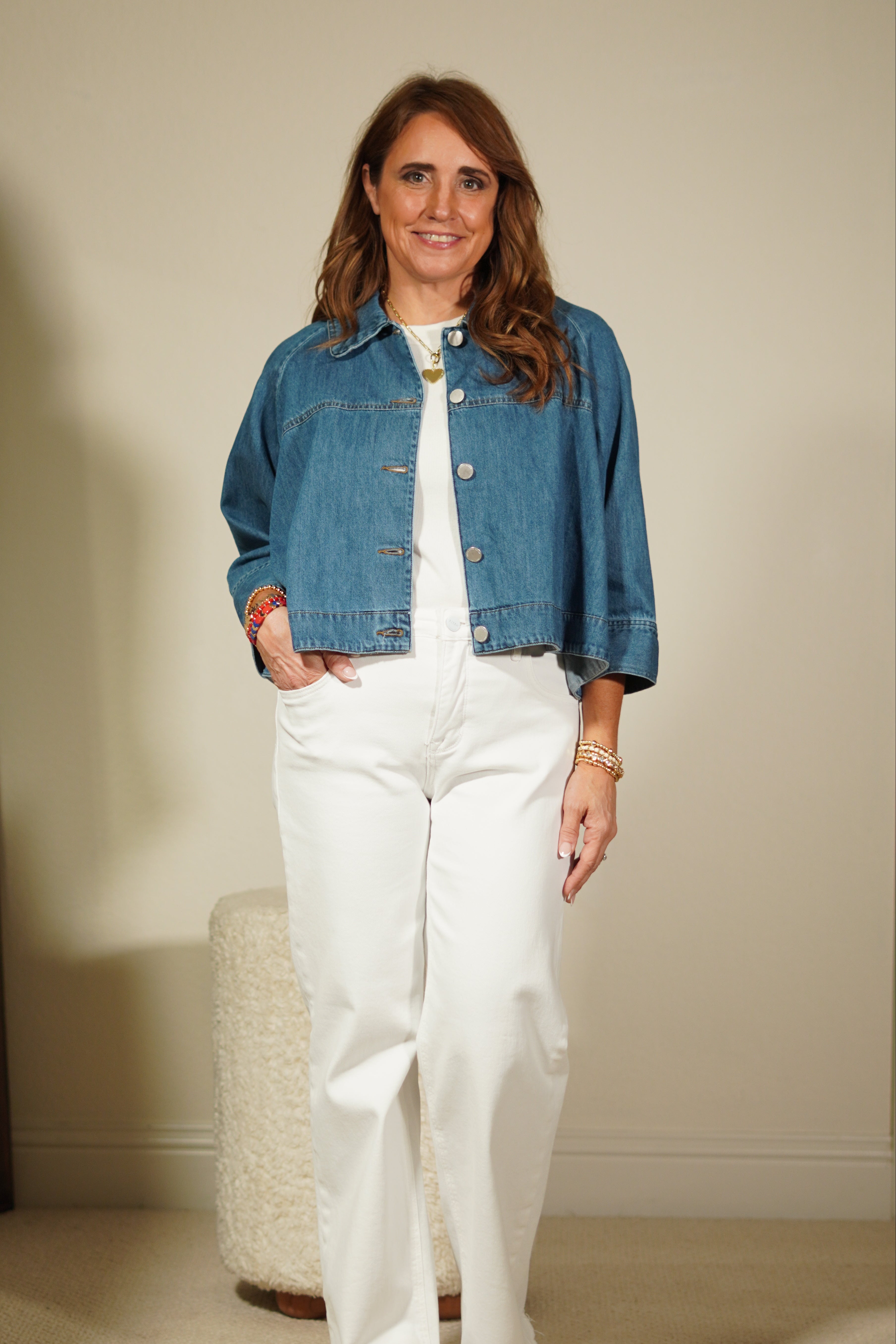 Woman wearing a denim jacket and white pants standing in front of a mirror.