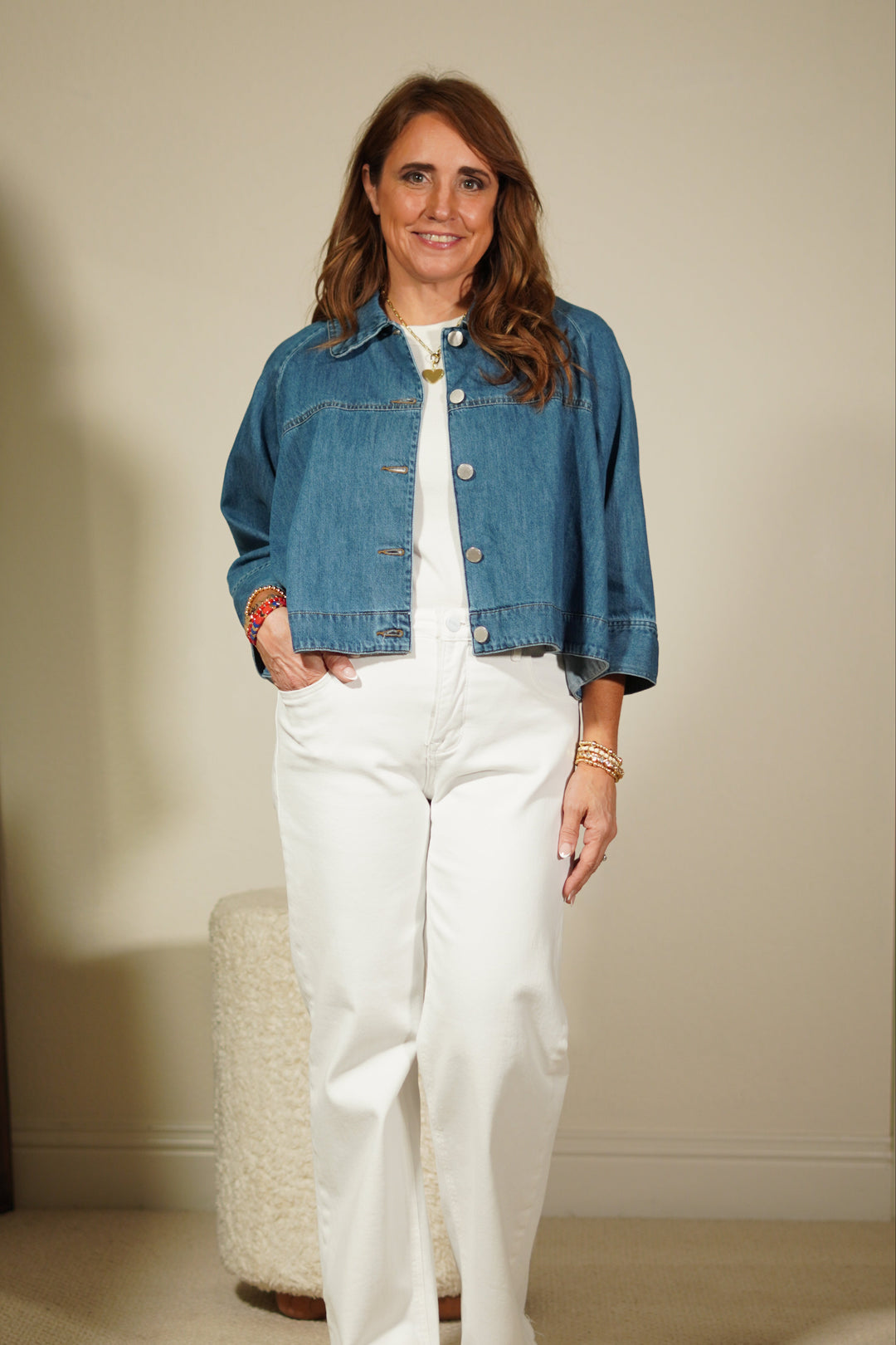 Woman wearing a denim jacket and white pants standing in front of a mirror.