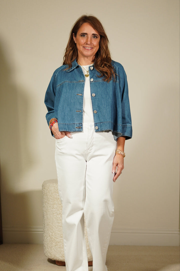 Woman wearing a denim jacket and white pants standing in front of a mirror.