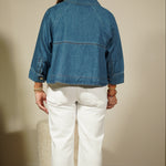 Person wearing a blue denim jacket and white pants standing in front of a mirror.