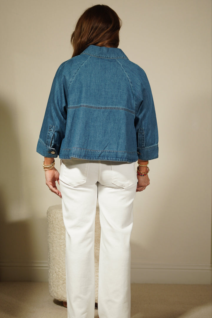 Person wearing a blue denim jacket and white pants standing in front of a mirror.