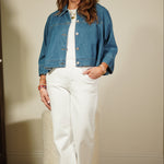 Person wearing a blue denim jacket over a white outfit, standing against a plain wall.
