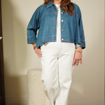 Woman wearing a blue denim jacket and white pants standing in front of a mirror.