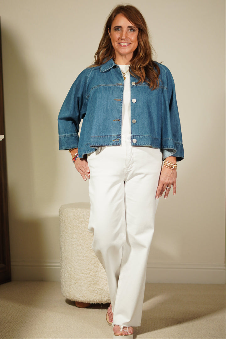 Woman wearing a blue denim jacket and white pants standing in front of a mirror.
