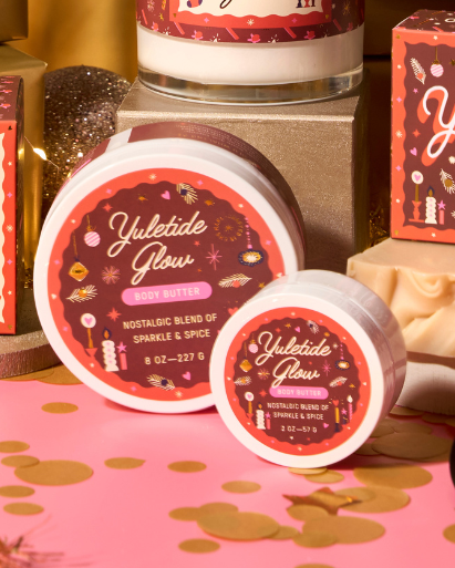 Yuletide Glow products including candles, bath bombs, and soaps on a decorative surface with festive lights.