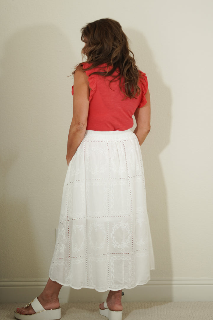 Woman wearing a red top and white skirt against a plain wall.