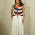 Woman wearing a sleeveless striped top with orange accents and a white skirt against a plain background