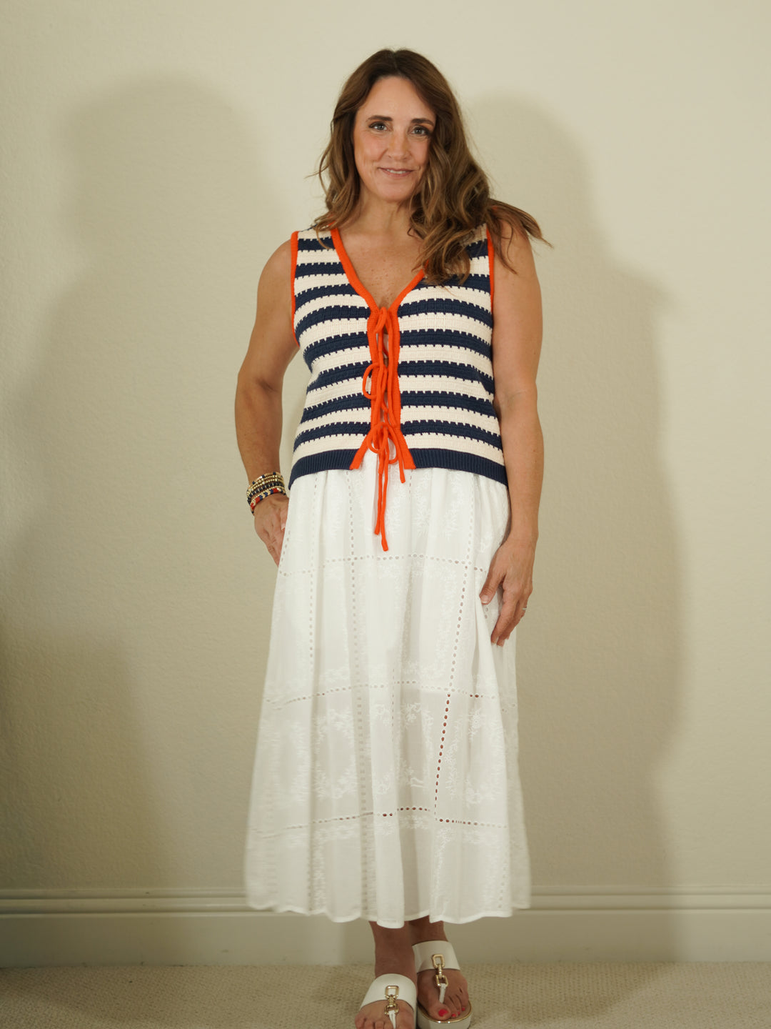Woman wearing a sleeveless striped top with orange accents and a white skirt against a plain background