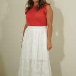 Woman wearing a red top and white skirt against a plain background