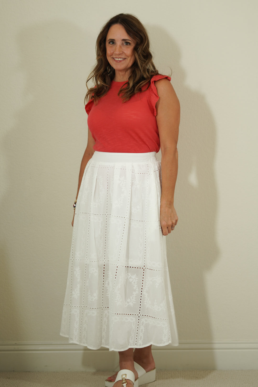 Woman wearing a red top and white skirt against a plain background