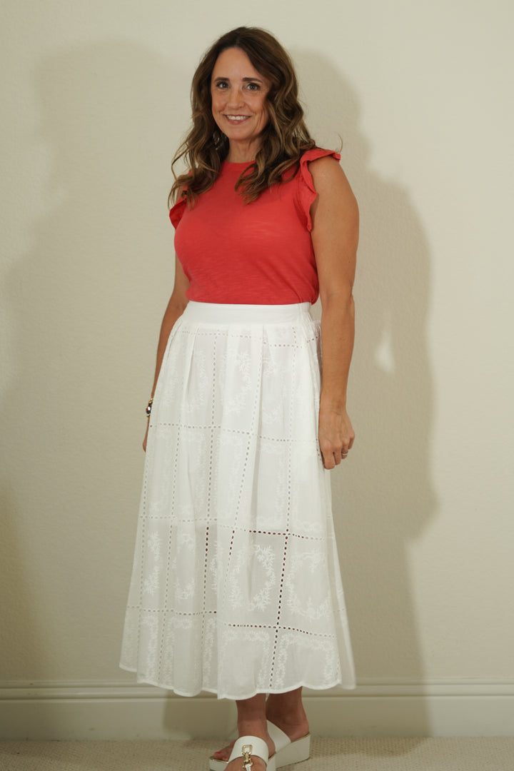Woman wearing a red top and white skirt against a plain background