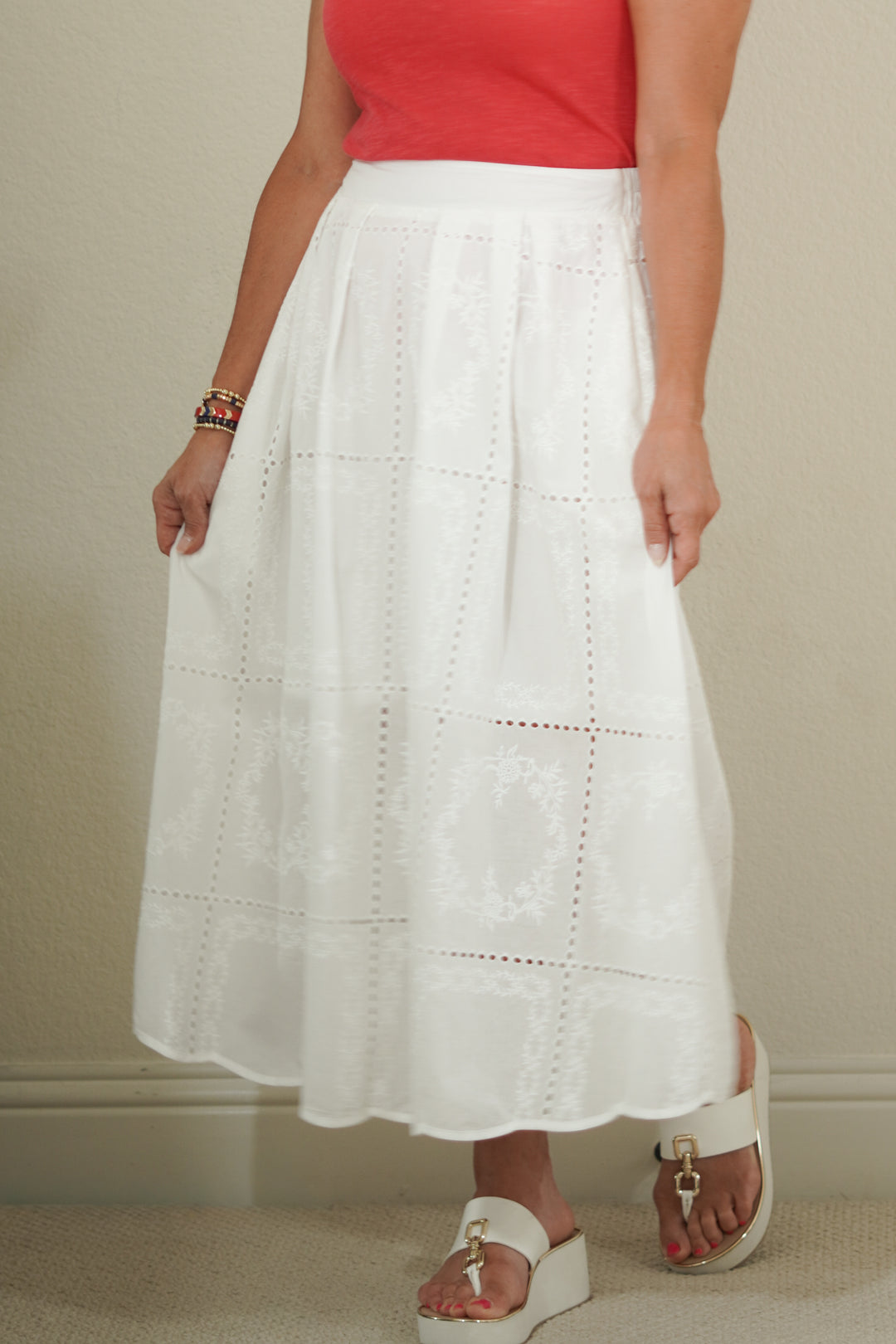 Person wearing a white skirt and red top against a neutral background