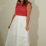 Woman wearing a red top and white skirt against a plain background