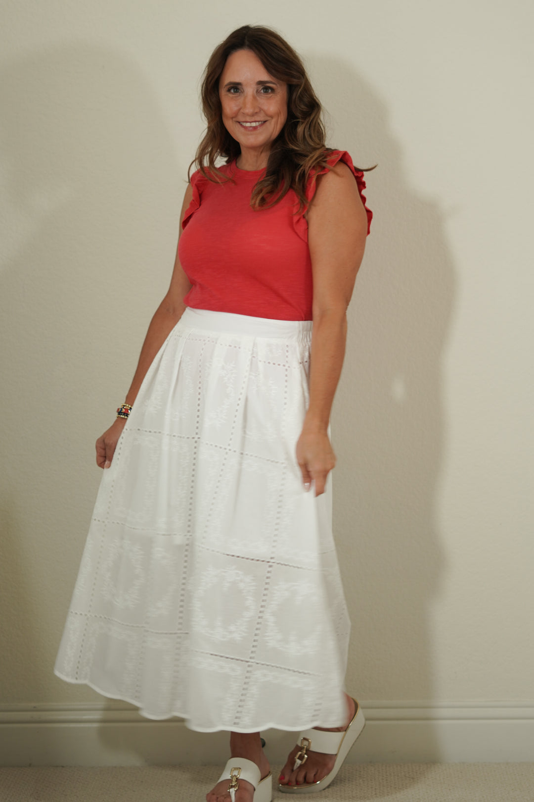 Woman wearing a red top and white skirt against a plain background